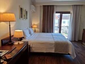 חדר מלון מודרני ונעים ליד שדה התעופה של אתונה, הכולל מיטה זוגית גדולה, ריצוף פרקט ומרפסת שמש ללינה נוחה ביוון.