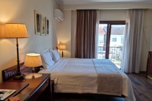 חדר מלון מודרני ונעים ליד שדה התעופה של אתונה, הכולל מיטה זוגית גדולה, ריצוף פרקט ומרפסת שמש ללינה נוחה ביוון.