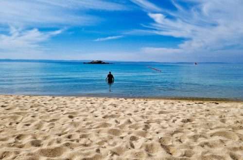 אדם שוחה במים צלולים ושקטים בחוף חולי זהוב ביוון