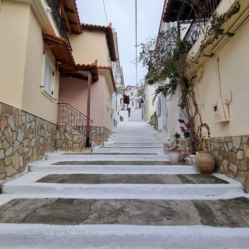 סמטה ציורית בעיירה קורוני (Koroni) עם מדרכות ומדרגות צבועות בלבן בוהק ובתים אותנטיים
