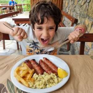 ילד רעב מחזיק את הסכום וממתין להתנפל על הצלחת שלו שיש בה נקניקיות, ציפס ואורז. ארוחה טובה אחרי מסלול הליכה מפרך בשמורת האולימפוס
