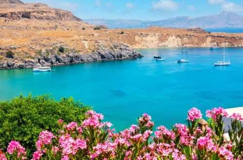 נוף פנורמי של מפרץ Lindos ברודוס עם מי טורקיז וסירות בים תחת שמיים כחולים