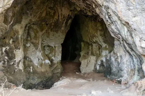 Close-up view of a natural cave entrance with rugged stone surfaces and earthy tones, showing weathered rock textures and a shadowy interior in Messenia, Peloponnese.