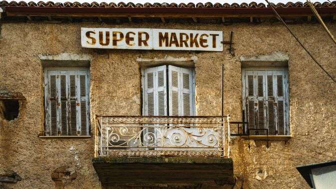 מבנה אבן מסורתי עם שלט סופרמרקט ישן ומרפסת ברזל בעיירה דלפי יוון.
