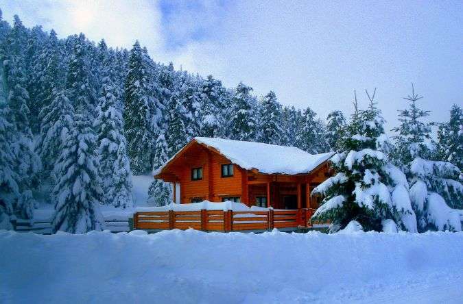 בקתת עץ מסורתית מכוסה שלג בלב יער אשוחים ליד אתר הסקי בהר פרנסוס, יוון.