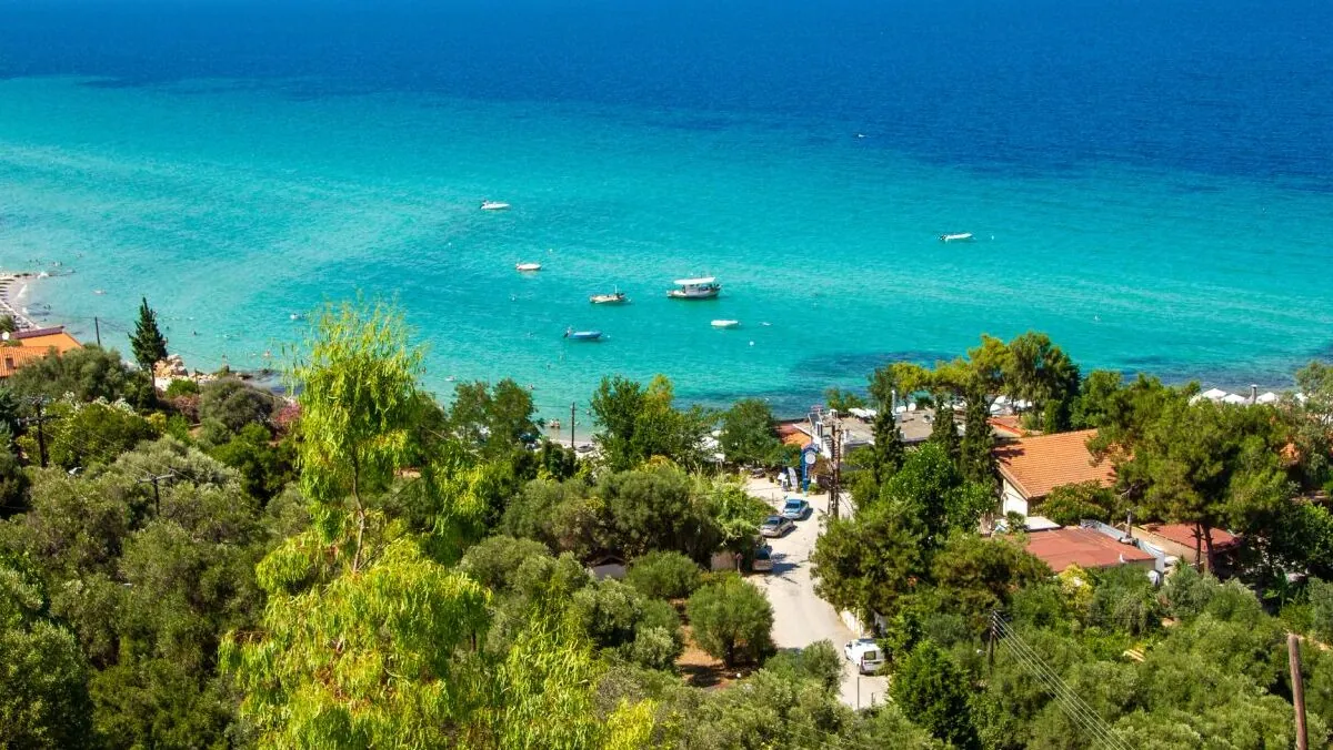 נוף ים כחול צלול עד האופק, ממרום הכפר ההררי אפיטוס בקסנדרה חלקידיקי, מוקף בעצים וטבע ובתים. מבט אל החוף למטה