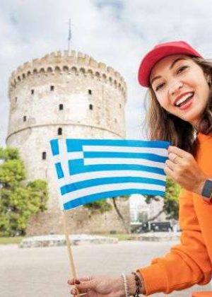 Happy student girl with a Greek flag on the background of a White Tower in Thessaloniki. The concept of citizenship or learning Greek language in university